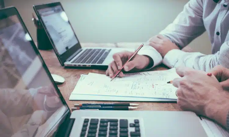 person holding pencil near laptop computer